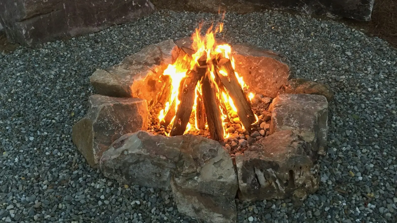 Loc de foc amenajat din pietre mari, pe pietriș, cu focul aprins